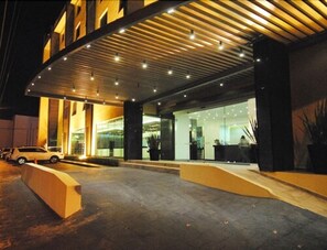 Entrada moderna de hotel com área externa coberta, balcão de recepção e um carro estacionado na frente.