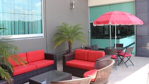 An outdoor seating area with red sofas, wicker chairs, and a table. - Hotel Ankara Las Lomas (San Luis Potosi)