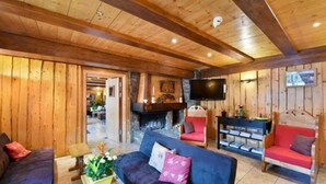A cozy living room with wooden walls and ceiling, a fireplace, a television, and comfortable seating. - Loc Hotel Alpen Sports (Les Gets)