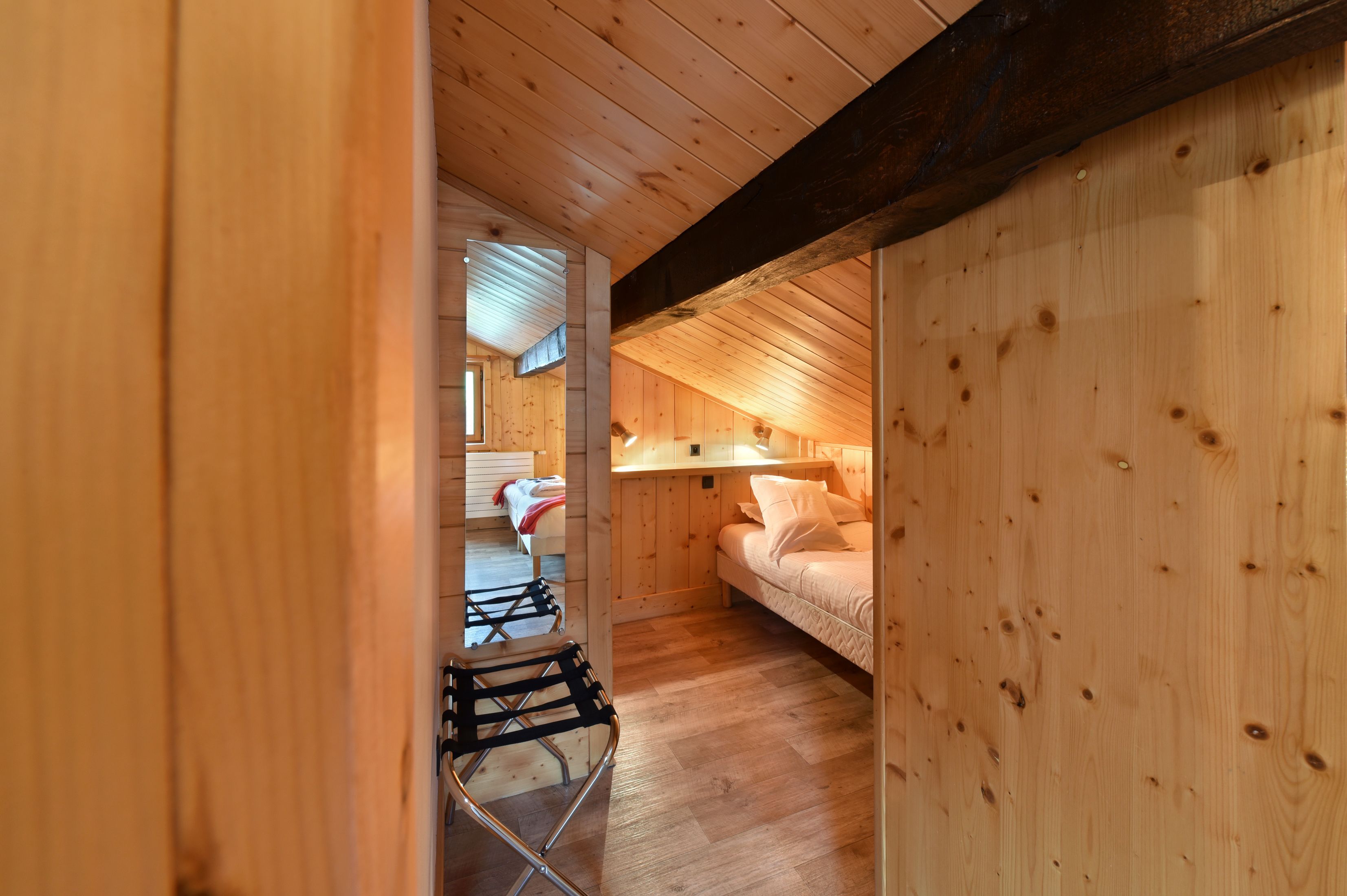 A wooden interior with a loft bed, a small table, and a chair.