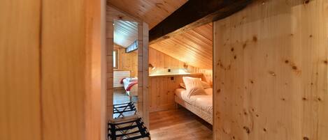 A wooden interior with a loft bed, a small table, and a chair.