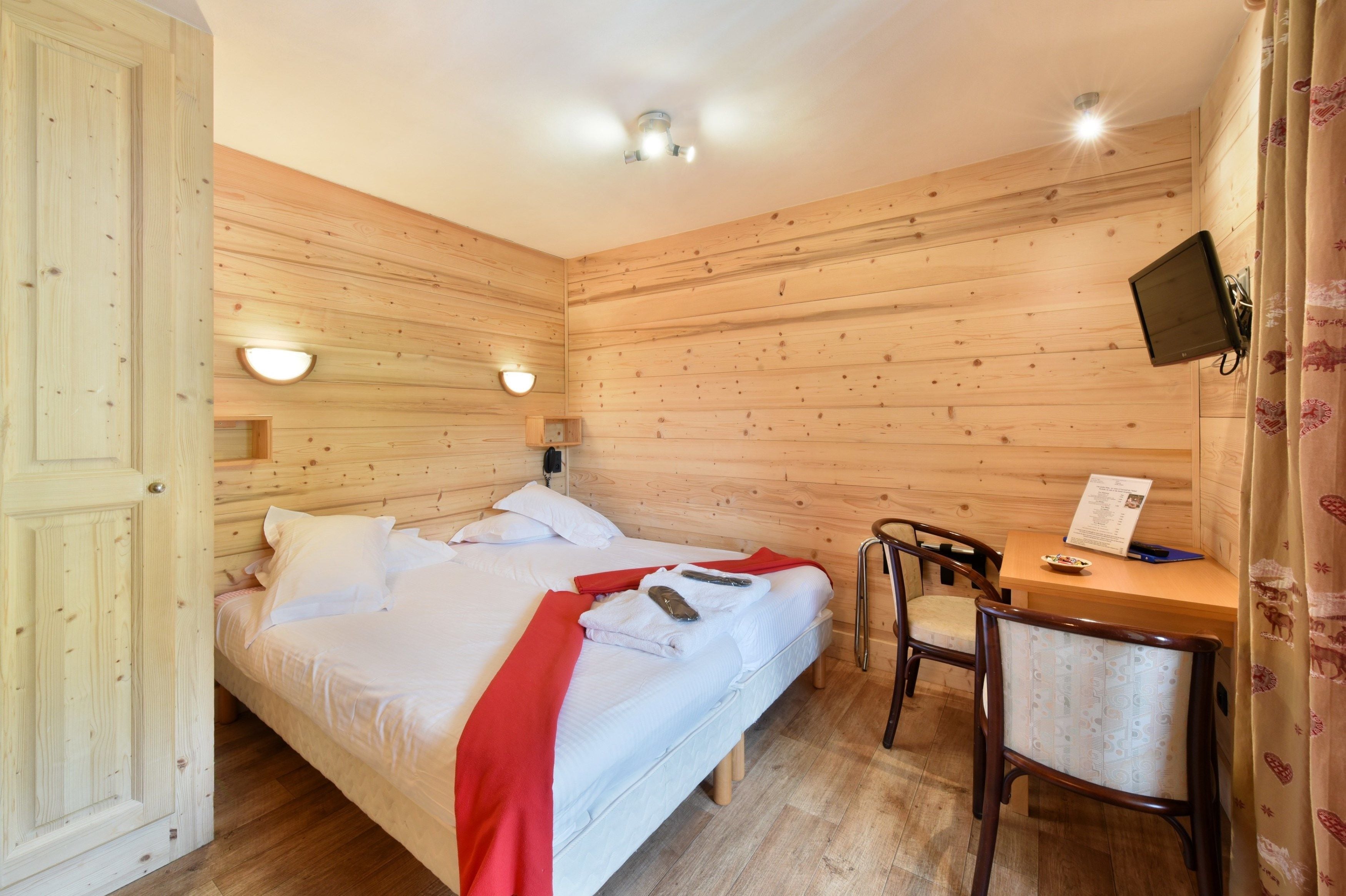 A wooden-paneled room with a bed, a desk, and a chair.