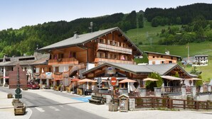 A wooden building with balconies, a sign reading "Jemine," and outdoor seating with umbrellas. - Loc Hotel Alpen Sports (Les Gets)
