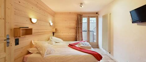 A wooden-paneled bedroom with a bed, a TV, and a window with curtains.