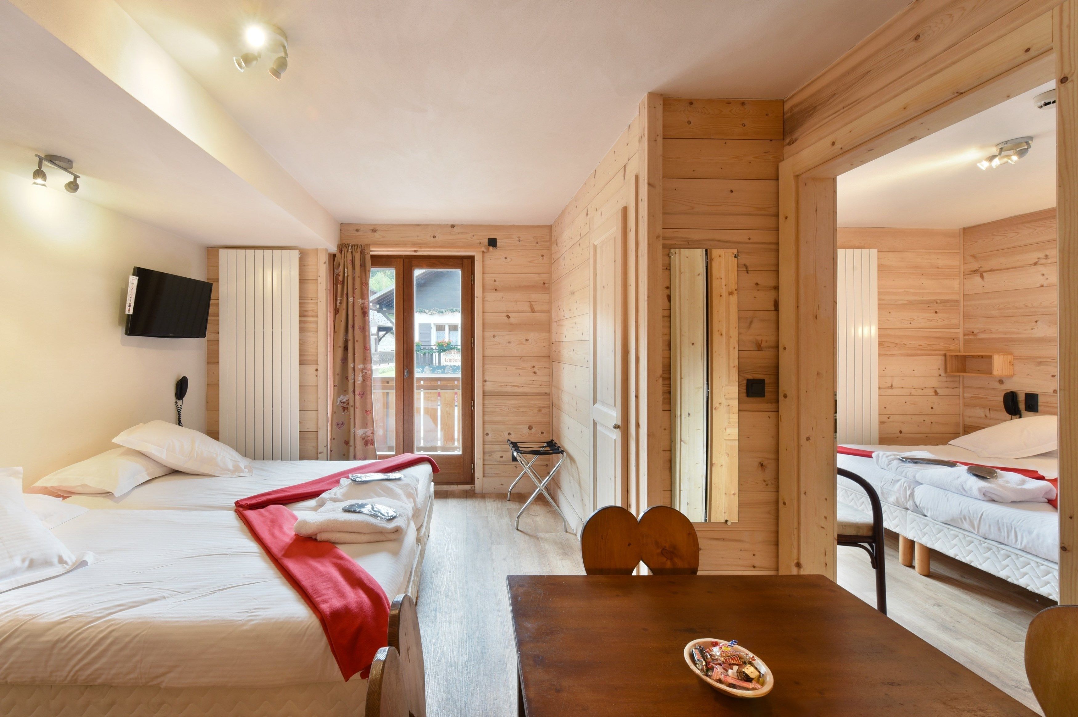 A wooden cabin with two beds, a dining table, and a TV mounted on the wall.