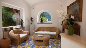 A room with wicker furniture, a tiled floor, a window with a view of greenery, and a painting on the wall. - Semiramis Hotel De Charme (Forio)