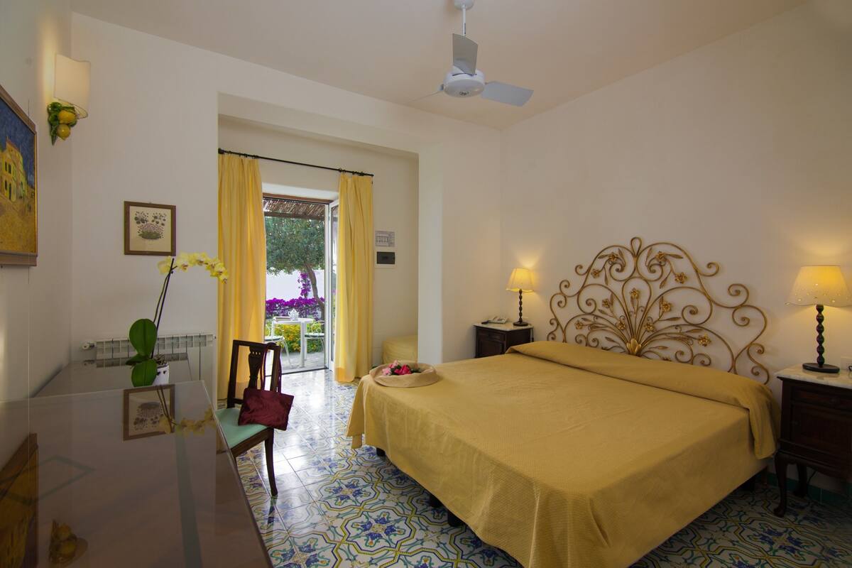 A hotel room with a bed, a desk, a chair, a nightstand, and a ceiling fan.