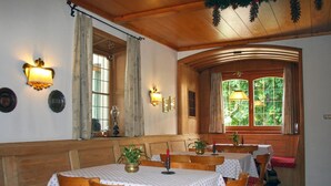 Comedor con mesas y sillas de madera, una lámpara de araña y un ventanal con cortinas.