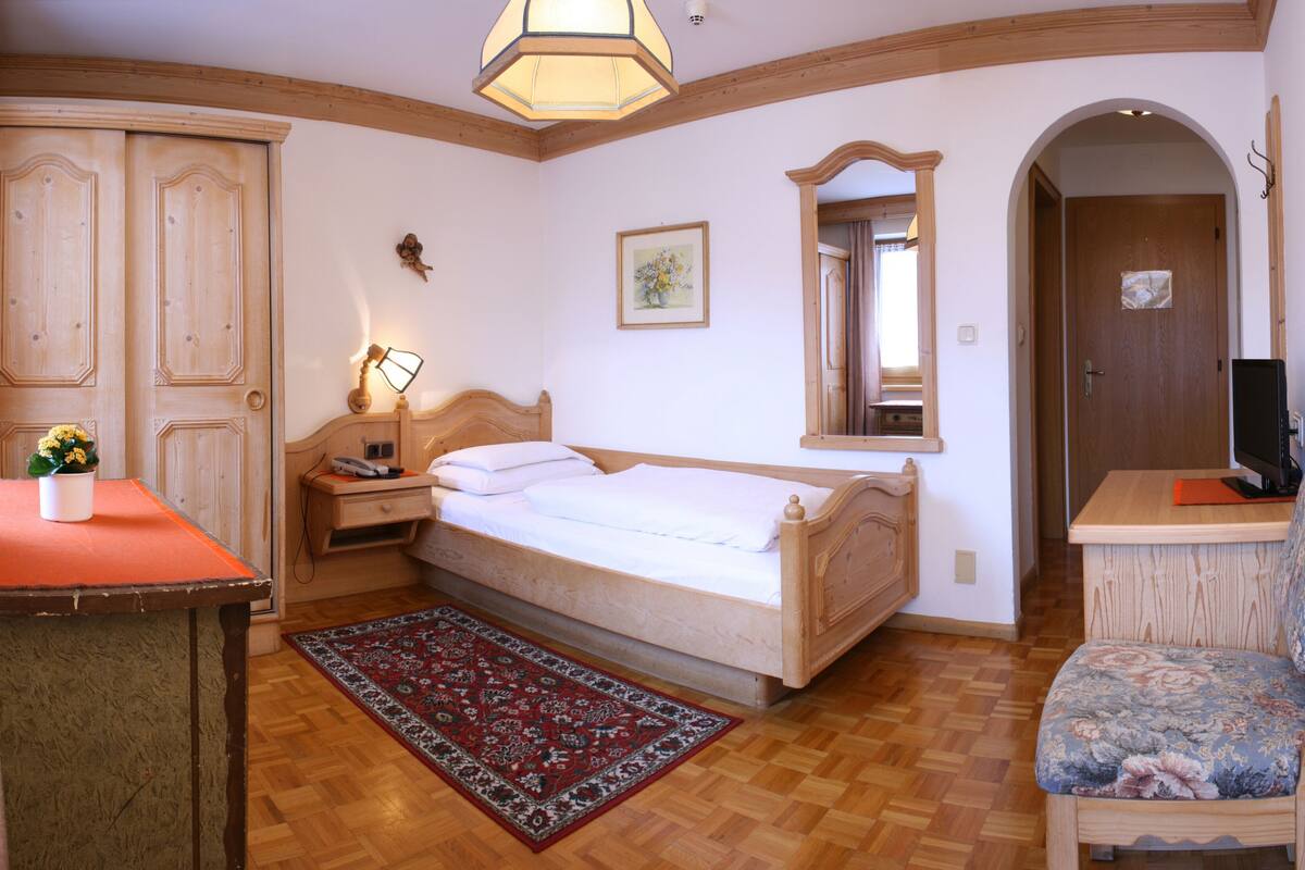 Un dormitorio con cama, mesita de noche, lámpara y una silla.
