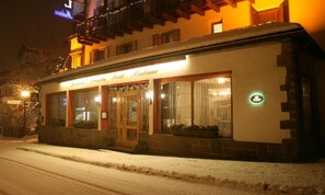 Un hôtel dont l’extérieur est recouvert de neige, une enseigne indiquant qu’il s’agit d’un restaurant et une entrée bien visible.