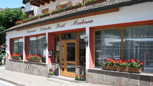 Restaurante y hotel llamado "Hotel Madonna" con fachada de piedra, ventanas de marco rojo y jardineras con flores.