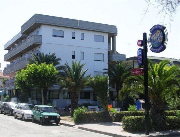 Un edificio de varios pisos con balcones, coches aparcados y palmeras.
