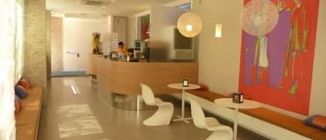 A modern hotel lobby with a reception desk, seating areas, and a large abstract painting on the wall.