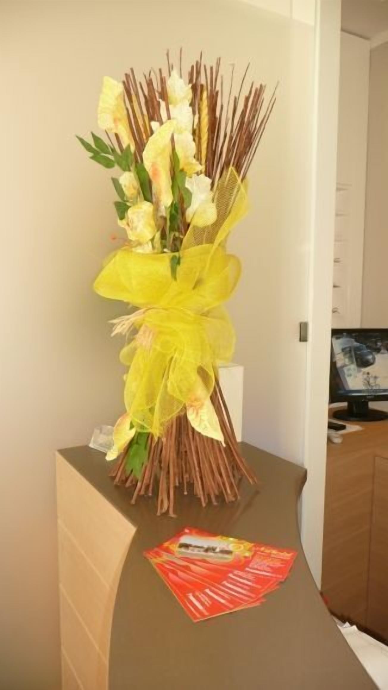 Een receptiebalie met een bloemstuk in een gele strik, een rode brochure en een houten kast op de achtergrond.