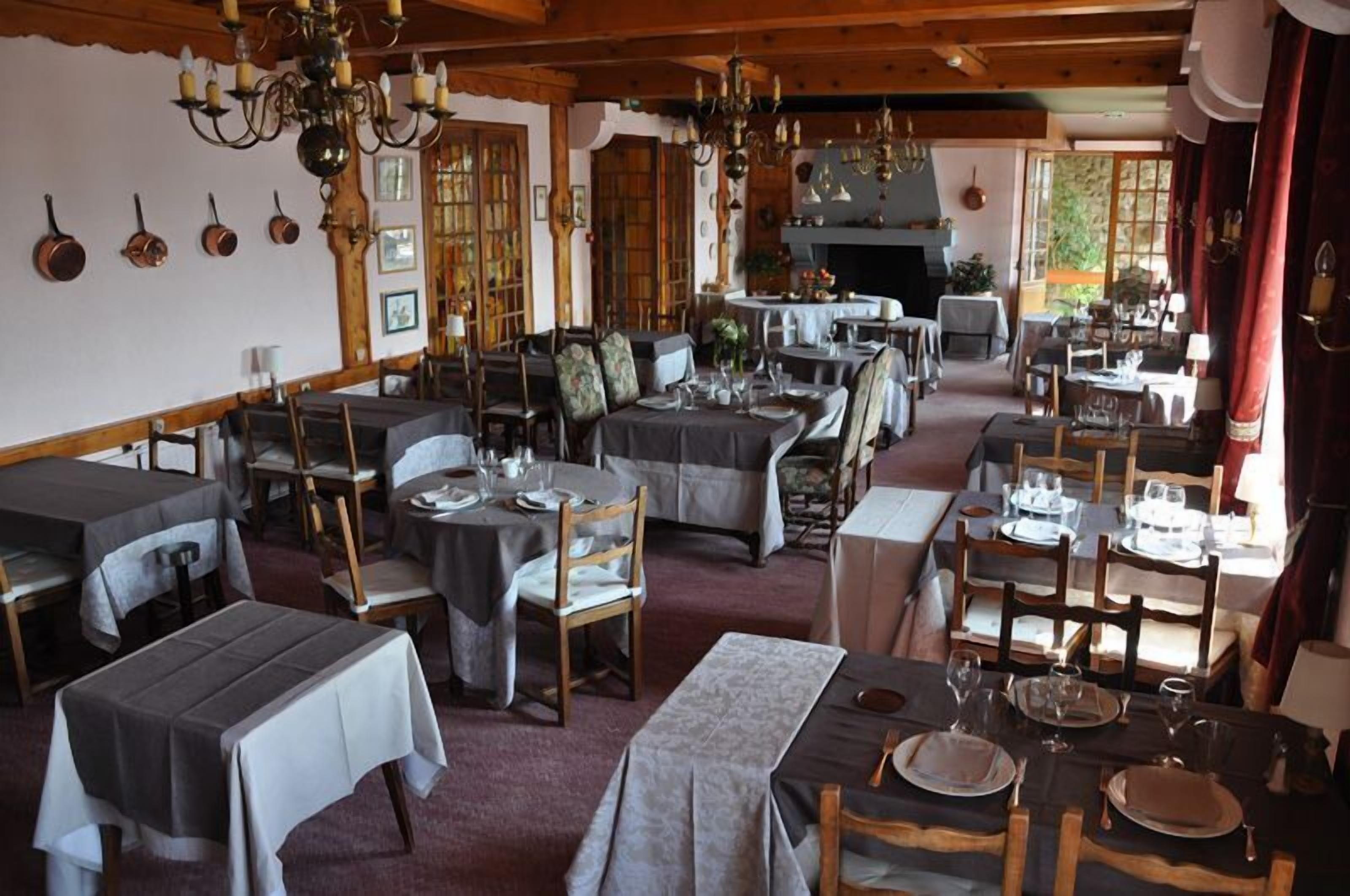 A dining area with multiple tables set for meals, wooden chairs, and chandeliers.