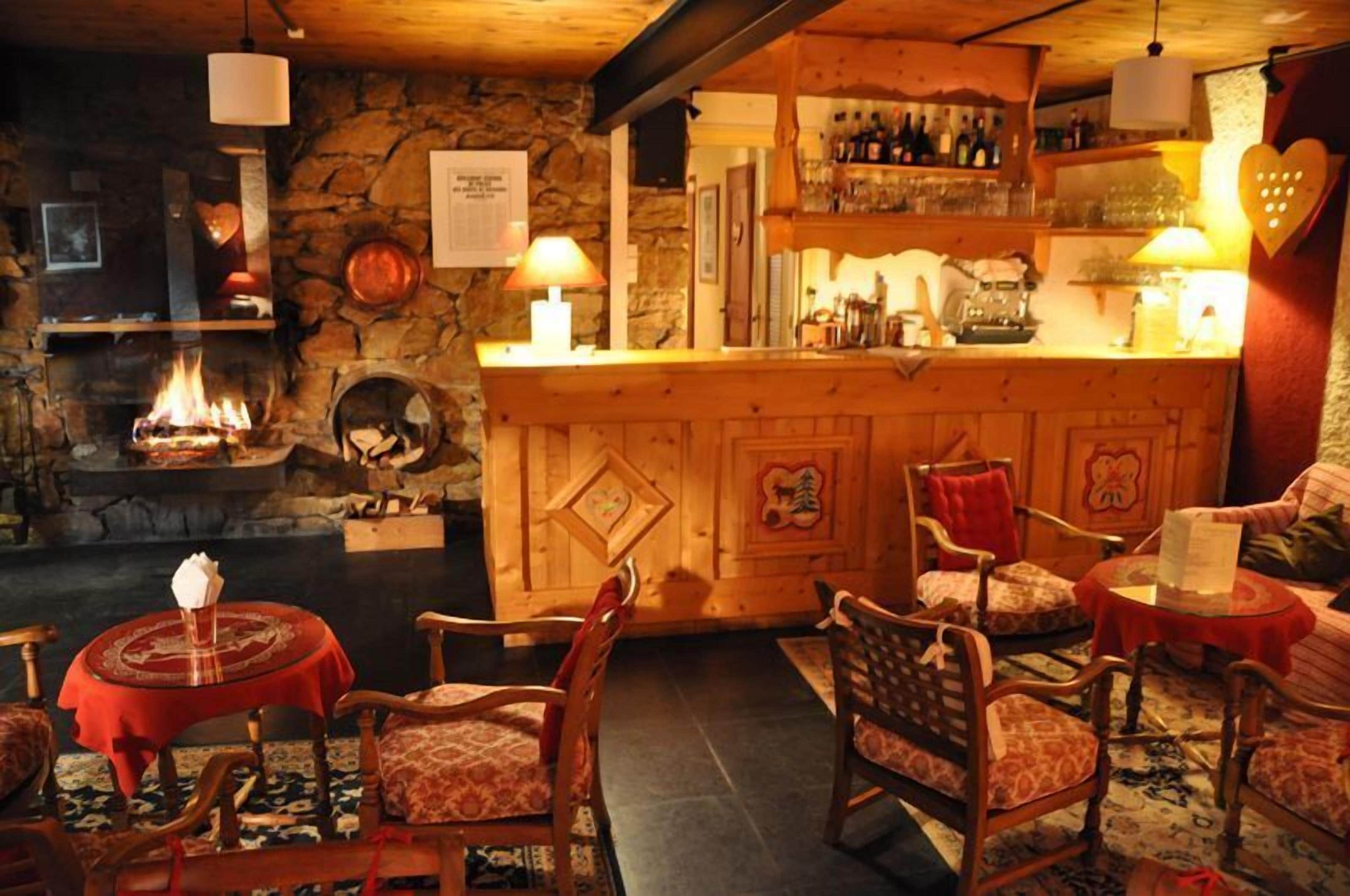 A cozy bar area with a stone fireplace, wooden furniture, and a bar counter with bottles and glasses.