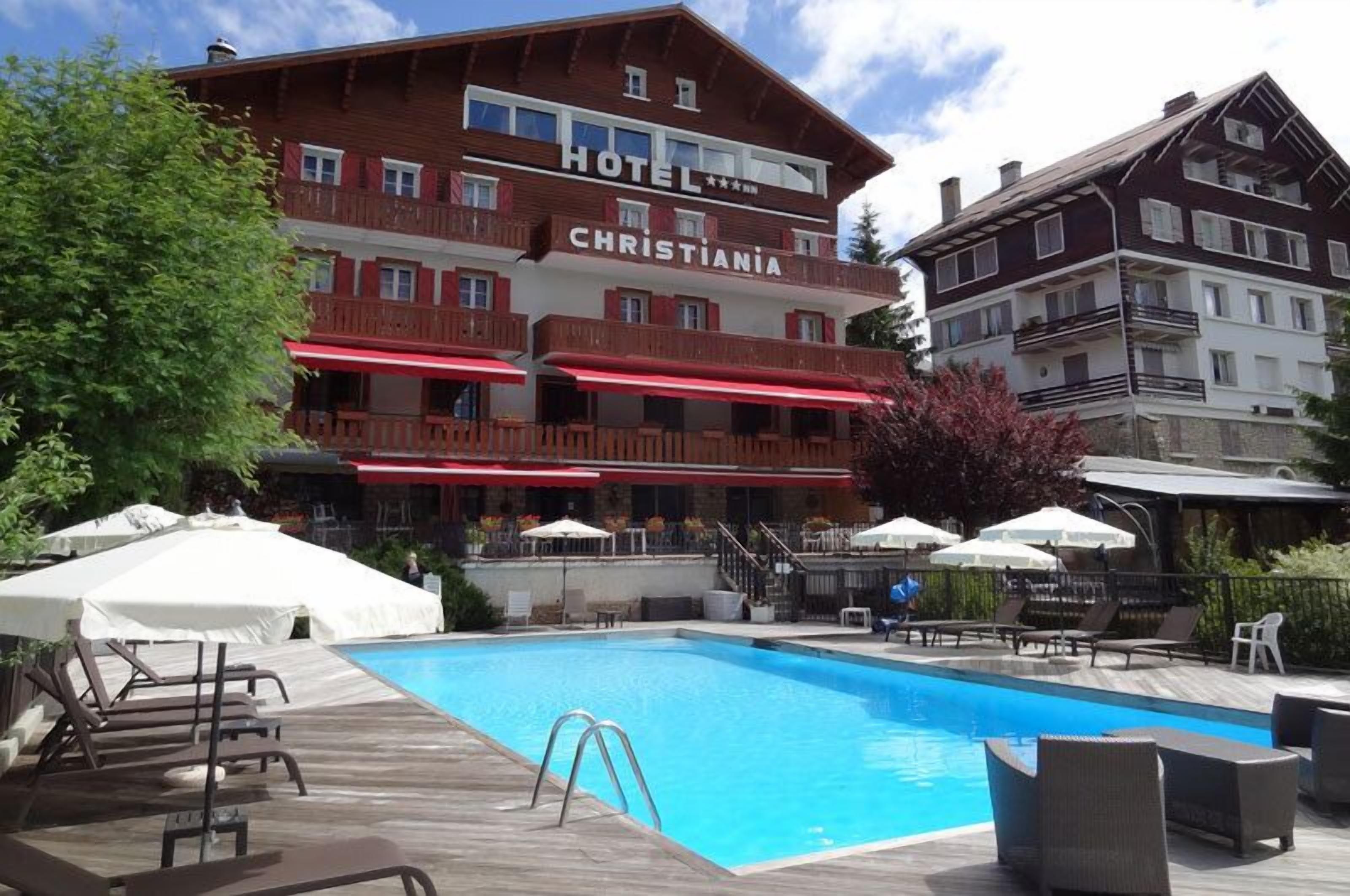 Un hotel llamado CHRISTIANIA con piscina, mobiliario exterior y terraza de madera.
