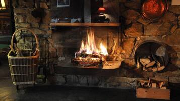 A stone fireplace with a fire burning, a basket of firewood, and a shelf with decorative items.