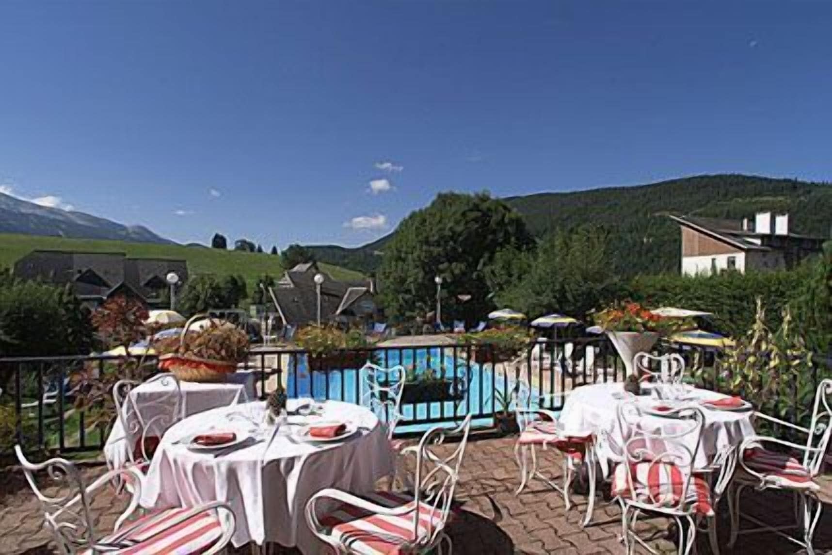 An outdoor terrace with tables and chairs, a pool, and a mountainous backdrop.