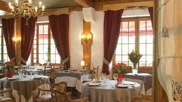A dining area with round tables, wooden chairs, and a chandelier.