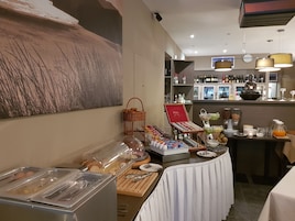 Ein reichhaltiges Frühstücksbuffet mit verschiedenen Speisen und Getränken, einer Weinauswahl und einer dekorativen Buddha-Statue.