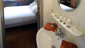 A hotel room with a bed, a bathroom with a sink and mirror, and a window with curtains. - Hotel Castel (Ghent)
