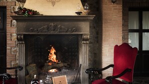 A fireplace with a fire, a red upholstered chair, and a table with a bottle, glasses, and a box of chocolates.
