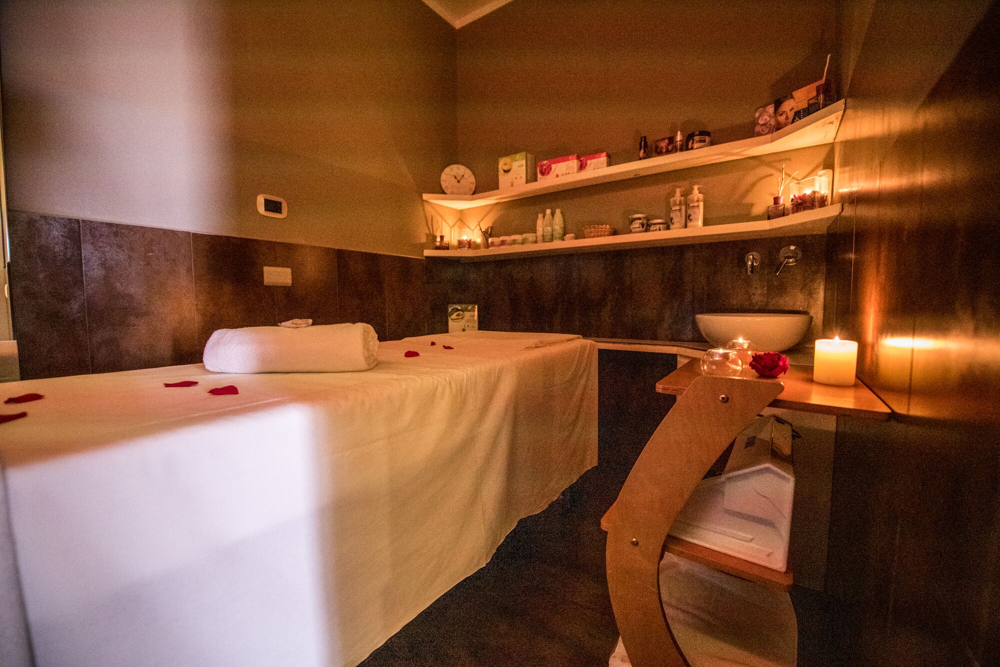 Et spa-rum med massagestol, lille håndvask, hylder med toiletartikler og et stearinlys.