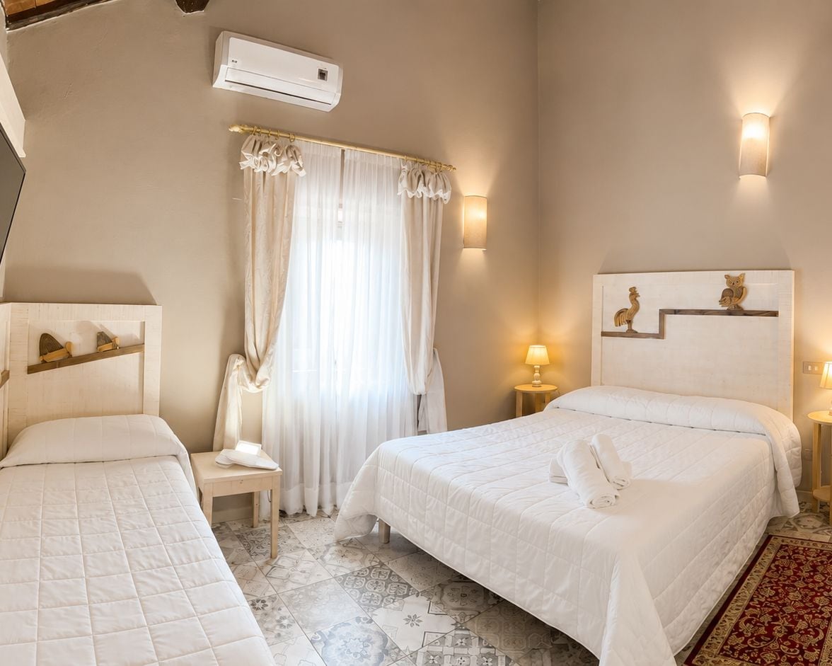 A hotel room with a bed, a chair, a nightstand, an air conditioning unit, and a window with curtains.