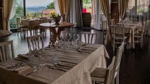 A restaurant with tables set for dining, large windows with curtains, and a view of the outdoors.