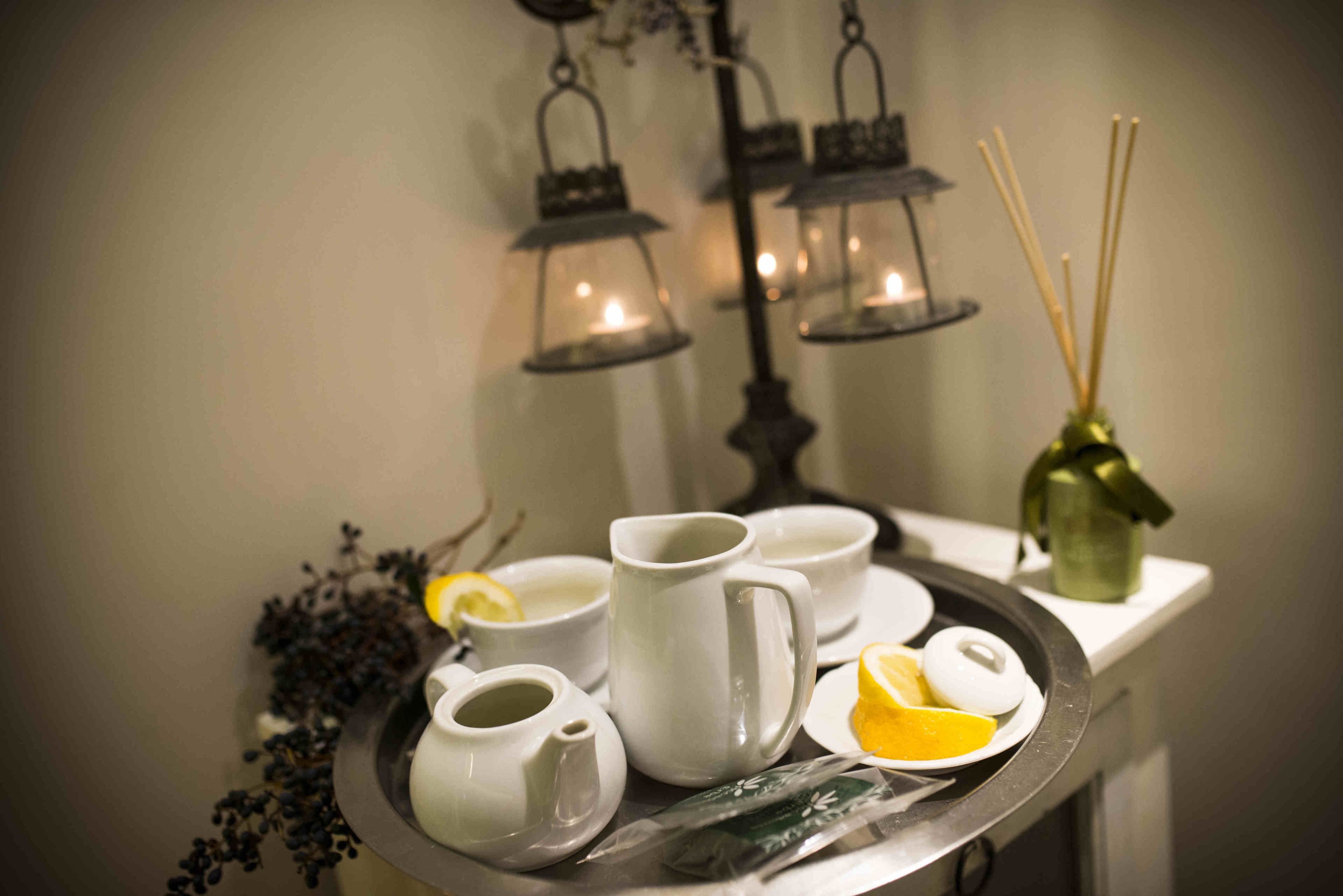 A tray with white teacups, a teapot, and lemon slices on a table.