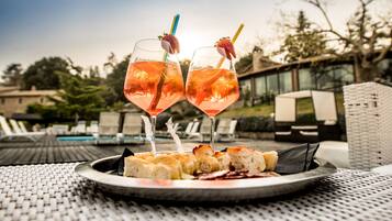 Dois copos de cocktail rosa com guarnições de fruta sobre uma mesa redonda com um prato de pão e queijo.