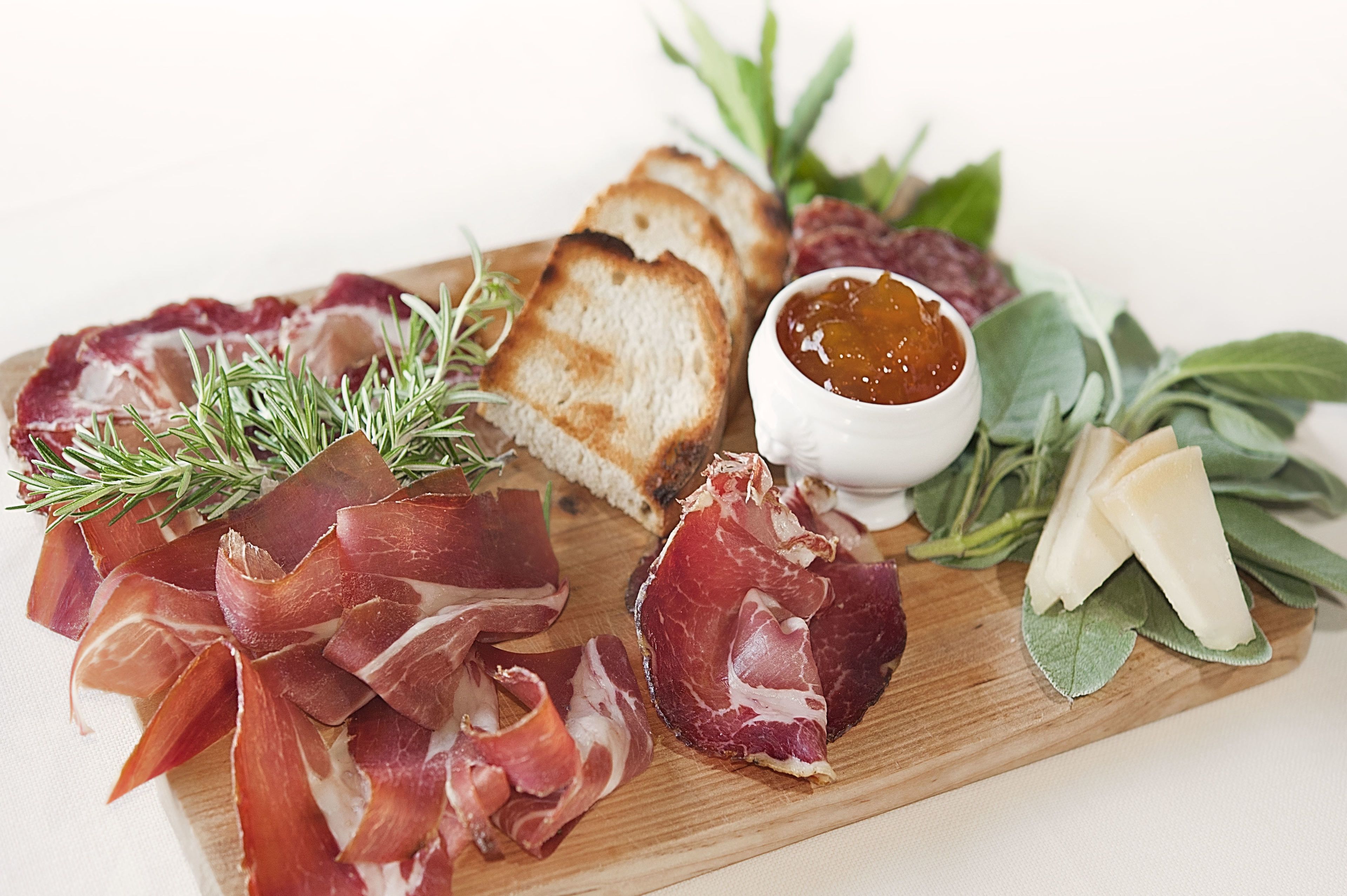 Una tabla de madera con diferentes carnes, pan y hierbas aromáticas.