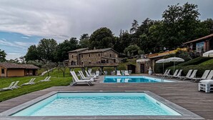 A pool area with two pools, lounge chairs, and a stone building with a balcony.
