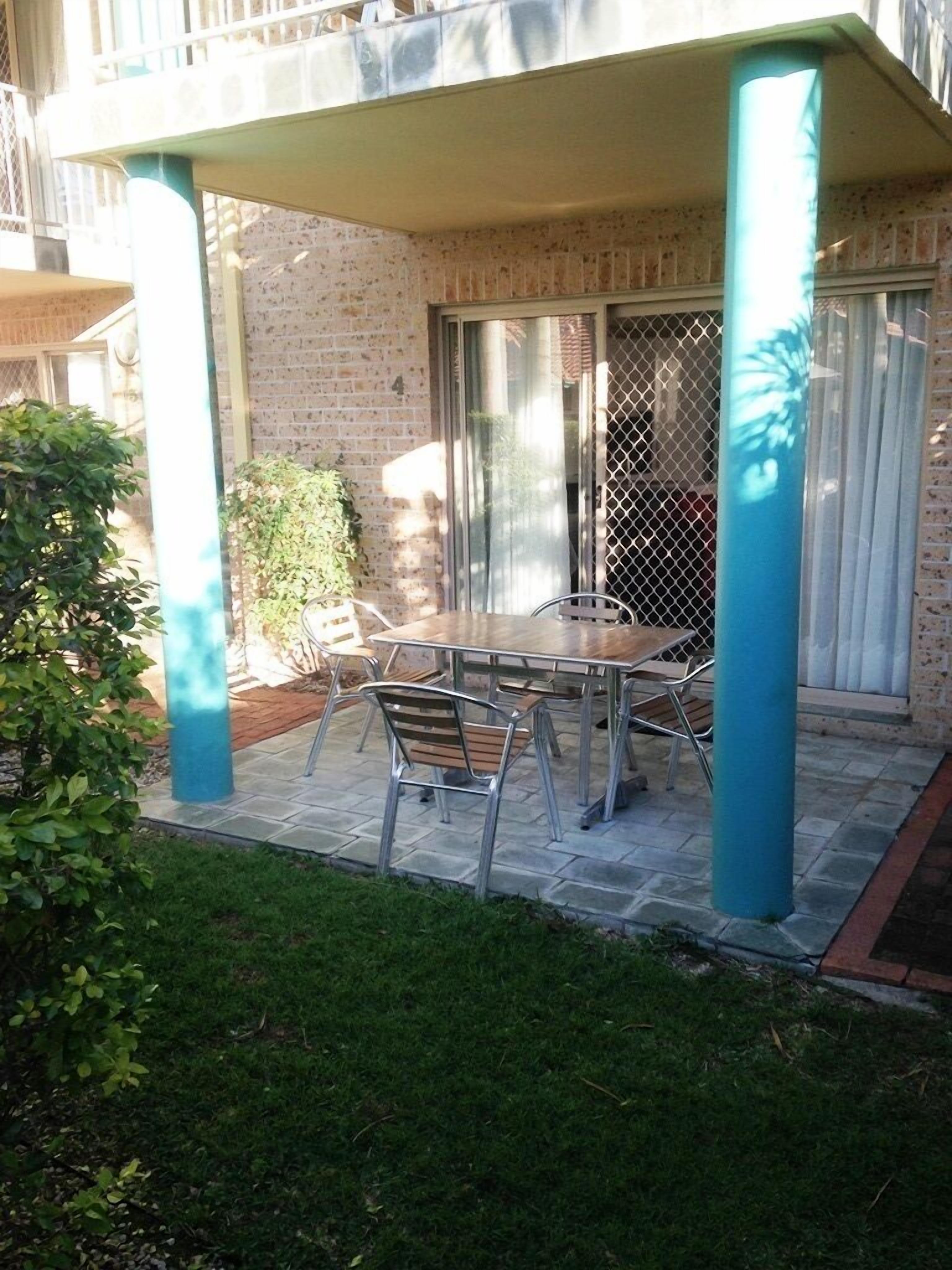A covered patio area with a table and chairs, a small garden, and a sliding glass door.