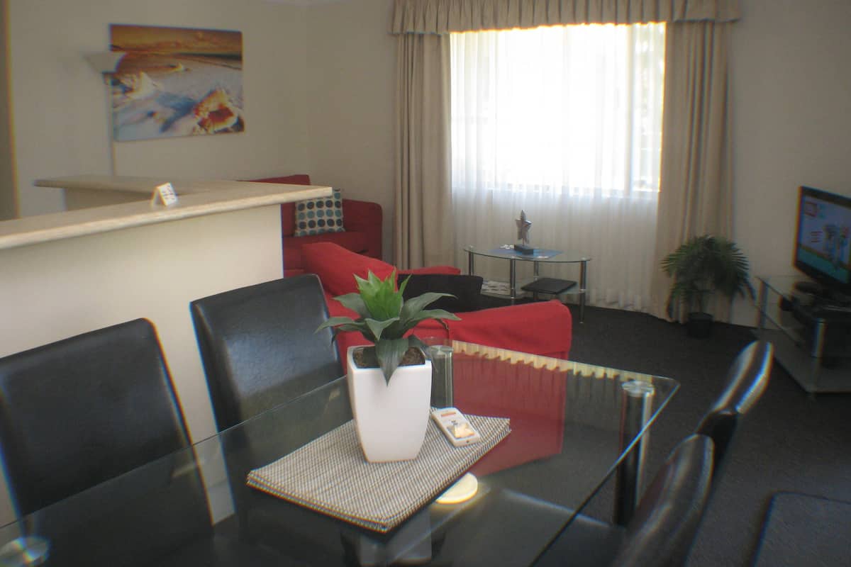 Ein Wohnzimmer mit Glastisch, rotem Sofa und einer Topfpflanze.