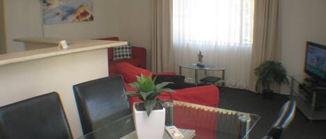 Un salon avec une table en verre, un canapé rouge et une plante en pot.
