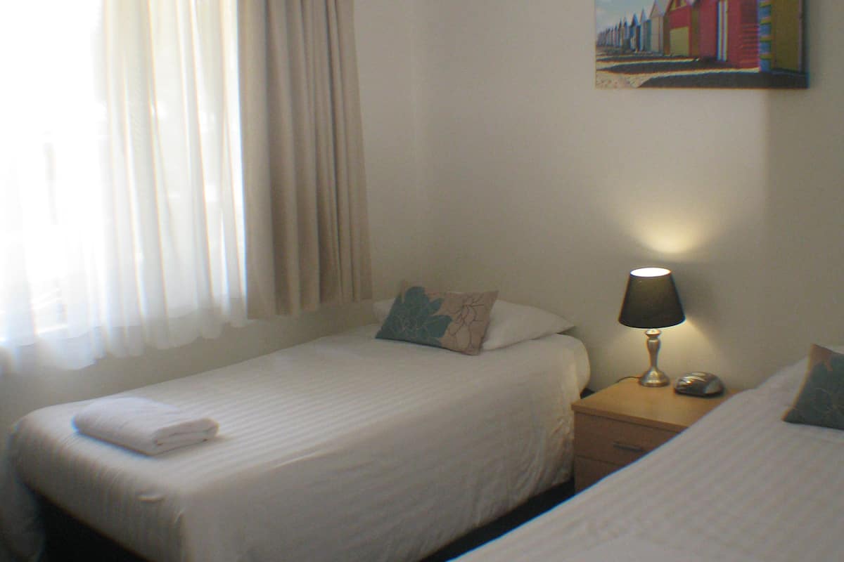 Ein Hotelzimmer mit zwei Einzelbetten, einem Deckenventilator, einem Bild an der Wand und einem Nachttisch mit Lampe und Telefon.