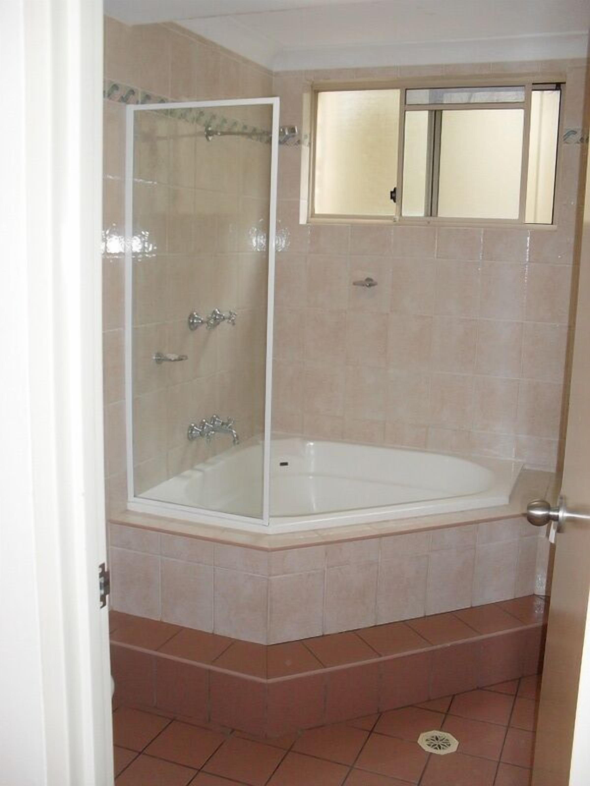 Une salle de bain dotée d’une douche à parois de verre, d’une baignoire et d’une fenêtre située au-dessus de la baignoire.