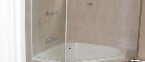 A bathroom with a glass-enclosed shower, a bathtub, and a window above the bathtub.