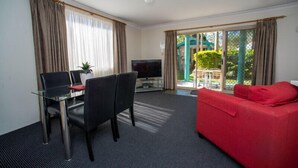 Una habitación de hotel con zona de comedor, un sofá rojo y televisión.