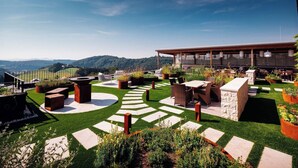 A rooftop terrace with outdoor seating, a modern building, and a scenic mountain view. - Genusshotel Riegersburg (Riegersburg)
