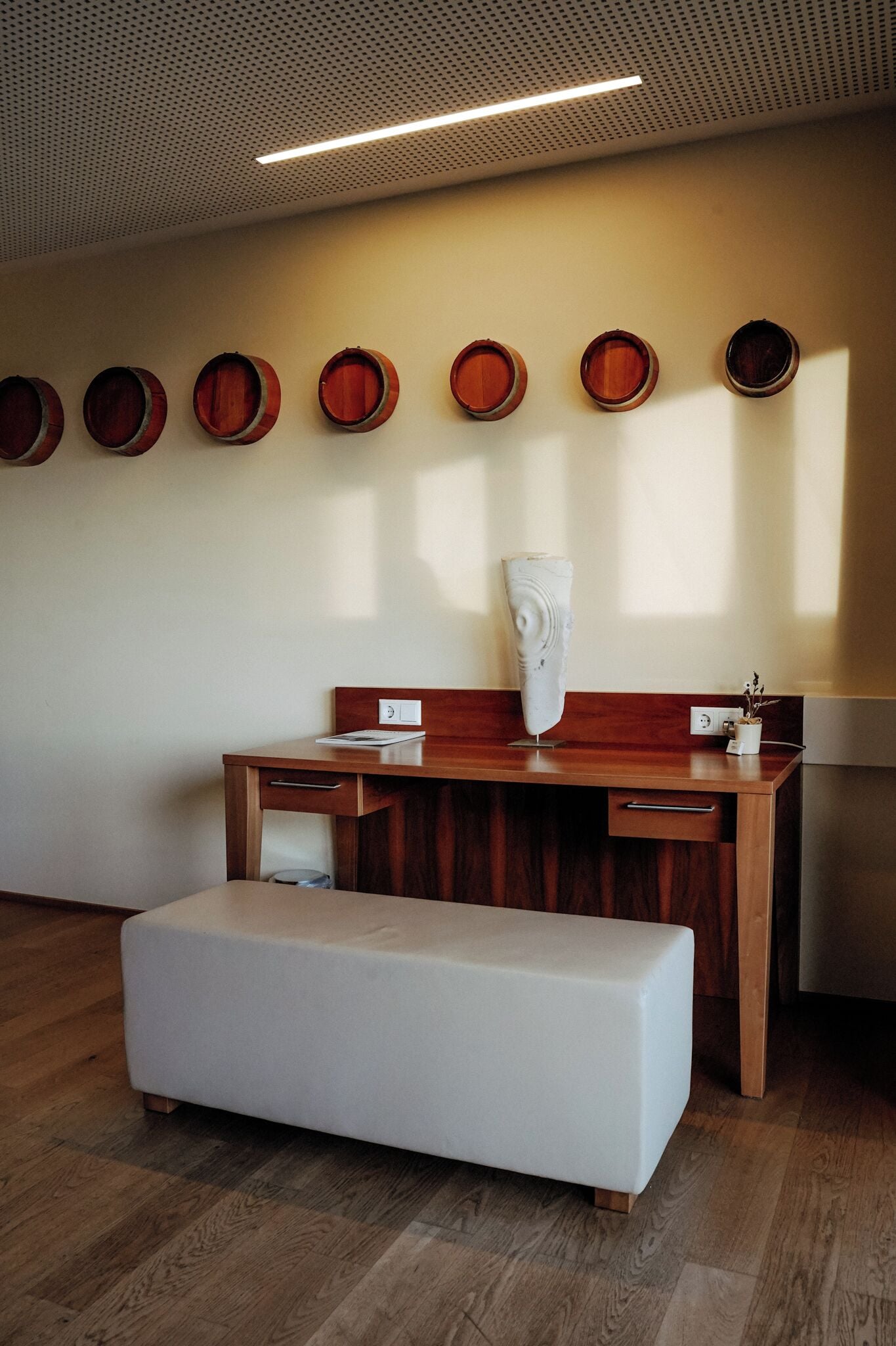 A room with a wooden desk, a white bench, and a wall with circular wooden objects.