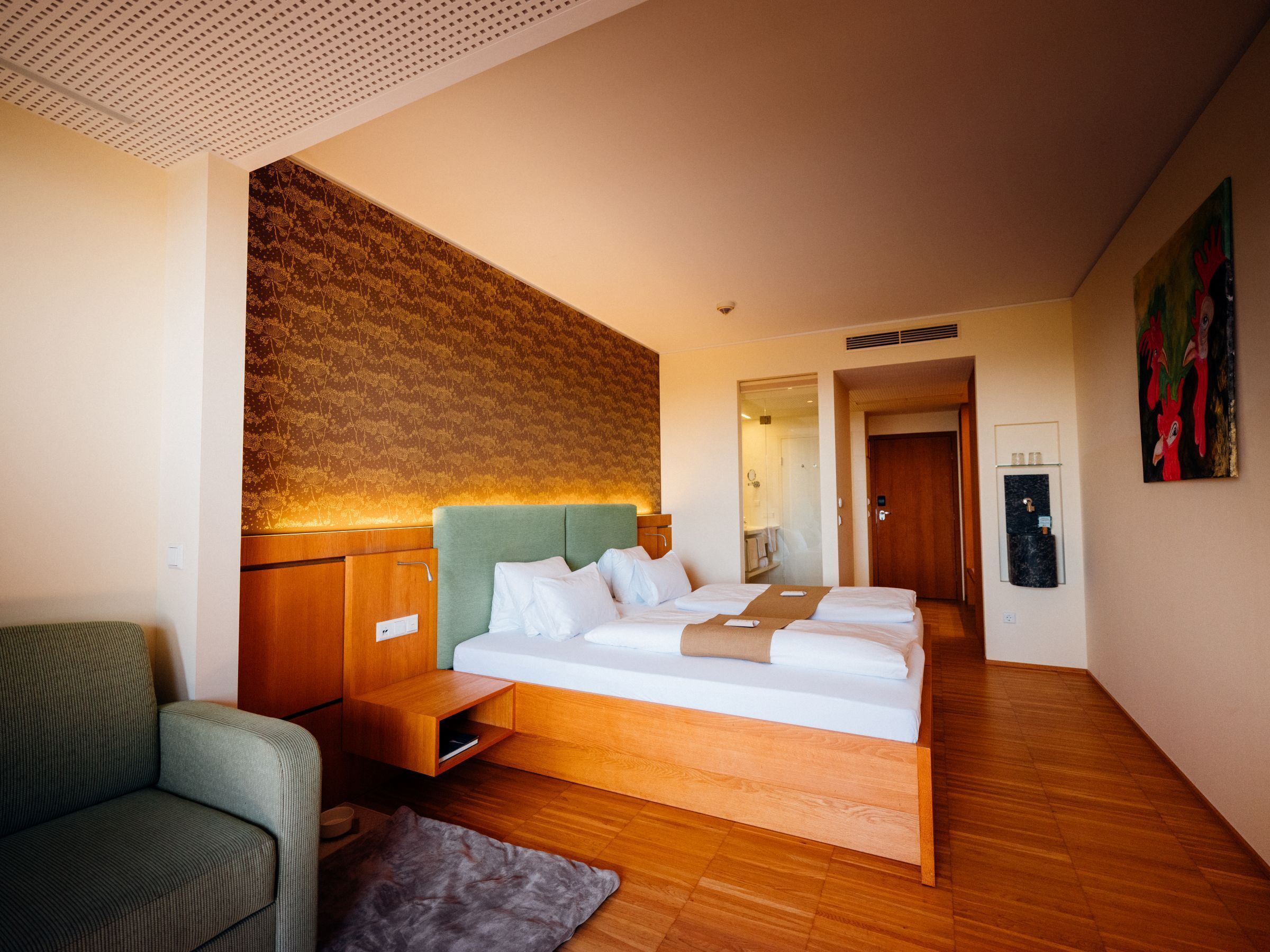 A modern hotel room with a large bed, a sofa, a wooden cabinet, and a decorative wall.