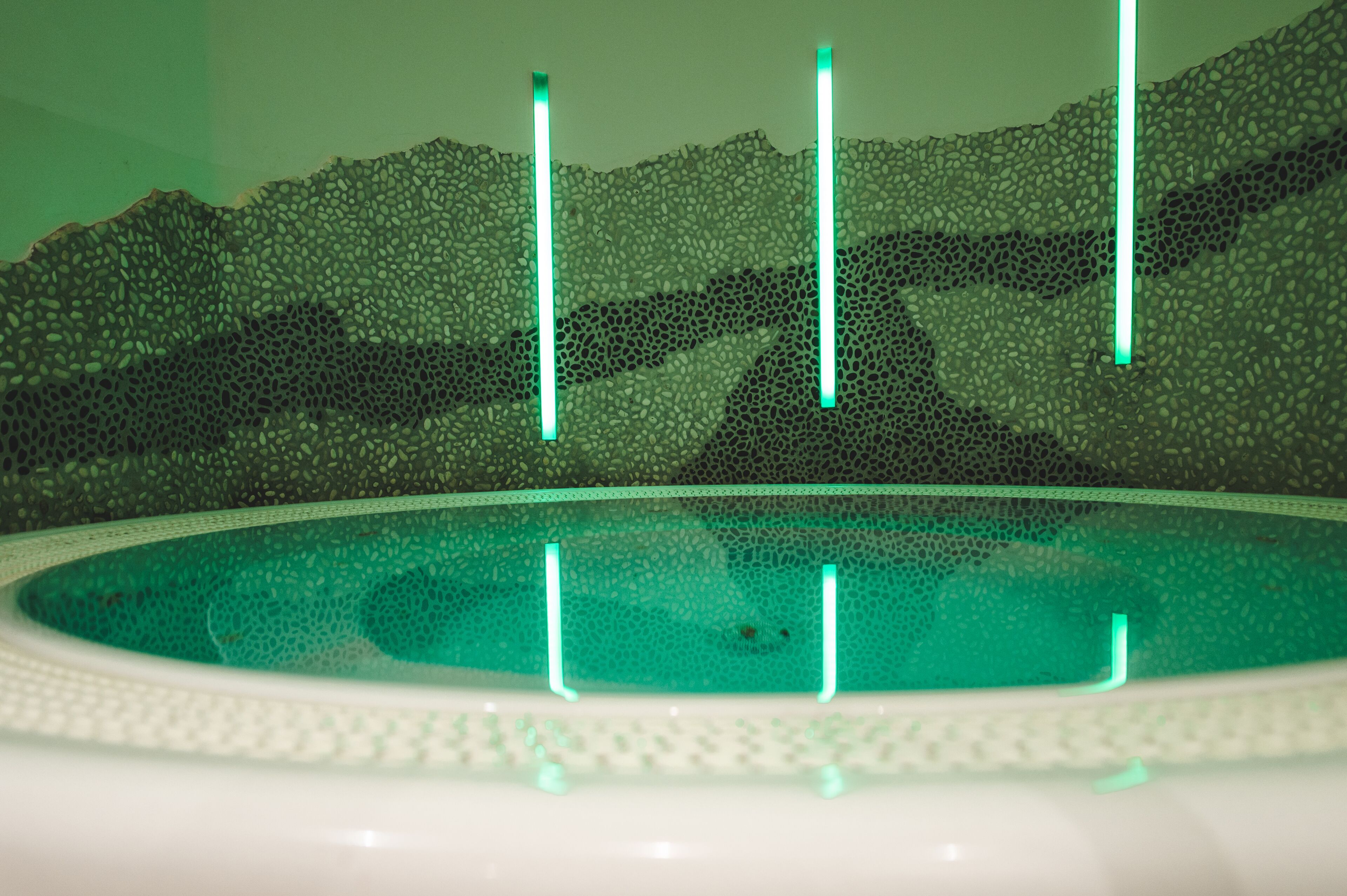 A close-up of a pool with a textured wall and four vertical light fixtures.