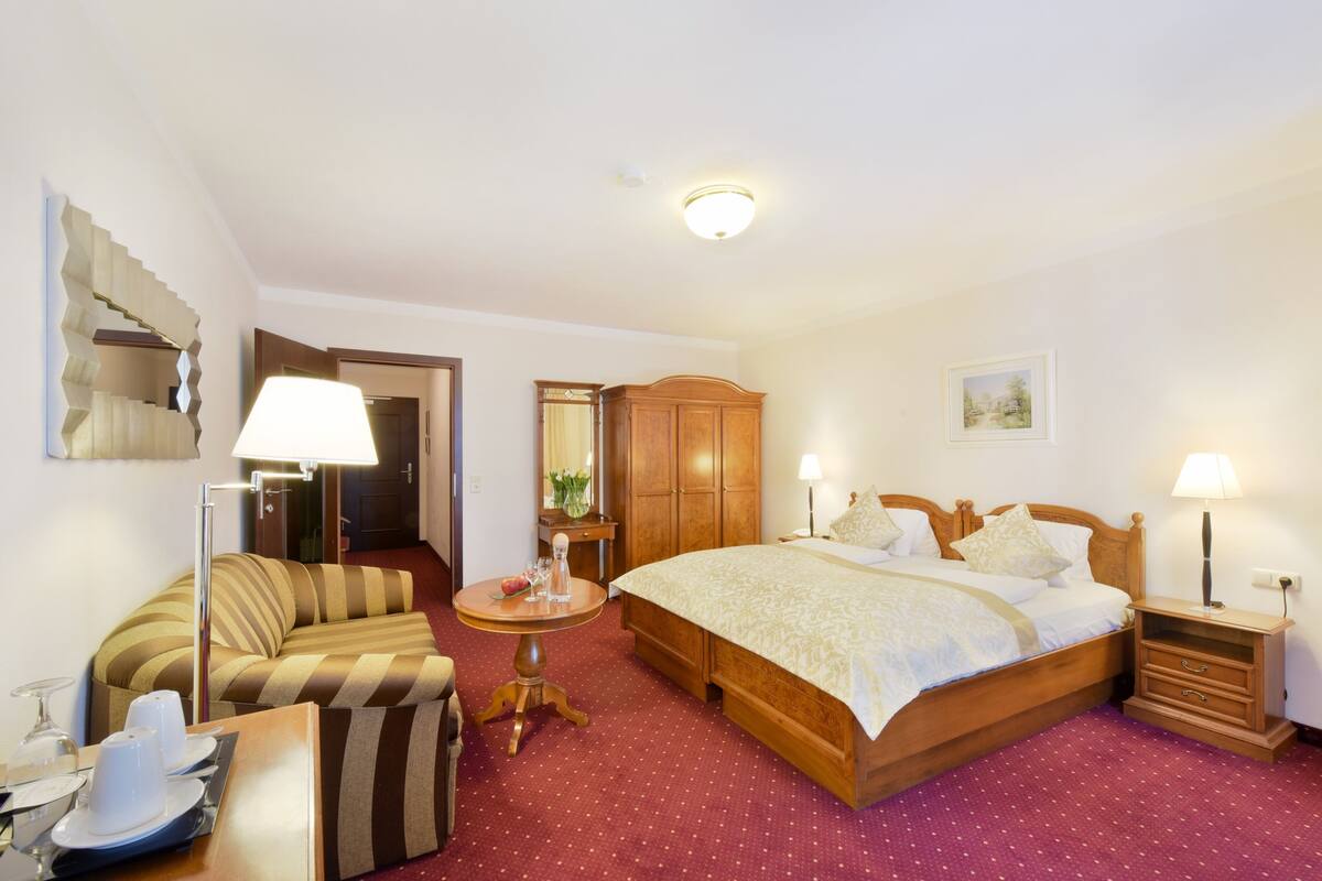 Une chambre d’hôtel avec un lit, un canapé, une petite table, un miroir et une armoire.