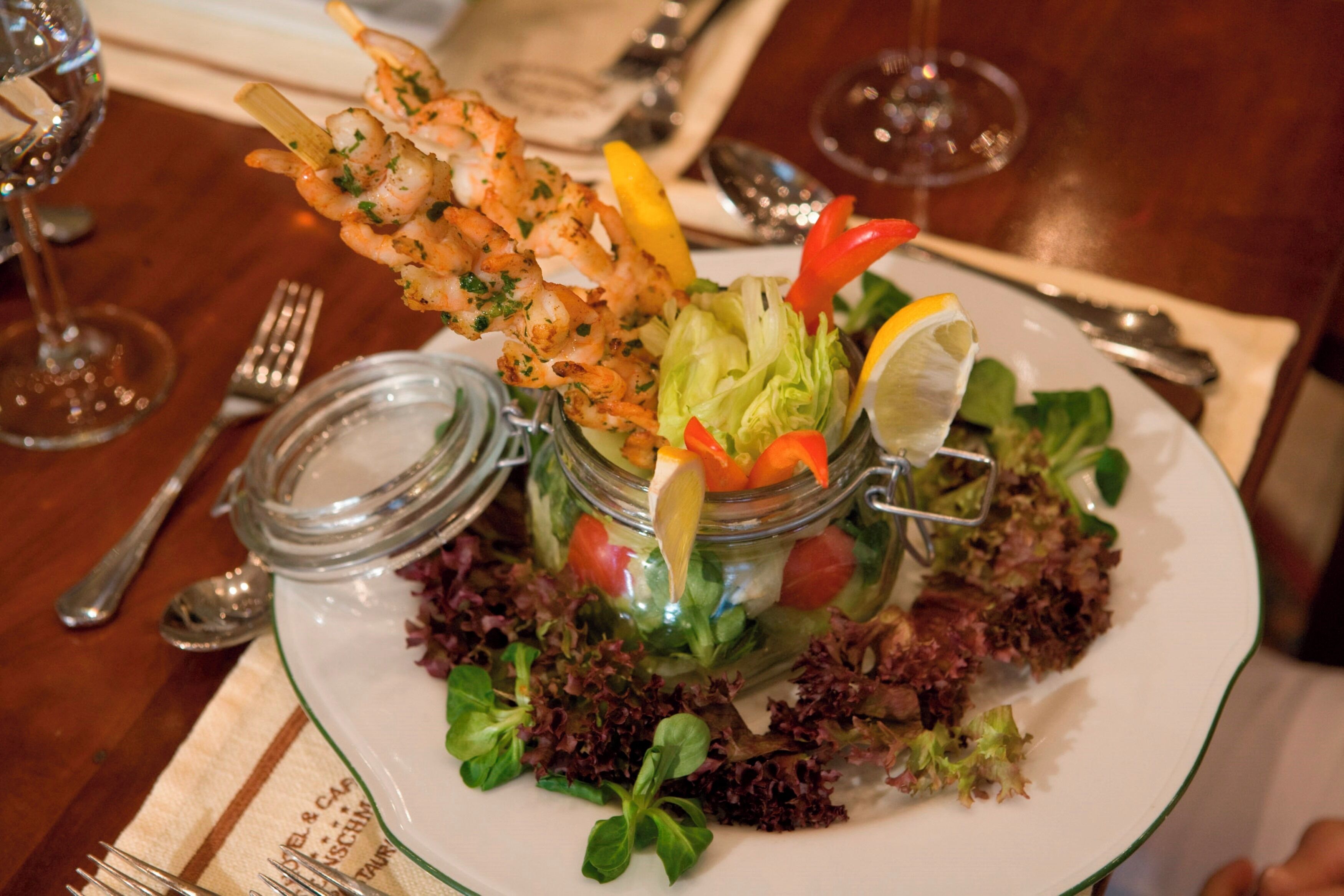 A plate of food with shrimp skewers, a salad, and a lemon wedge.