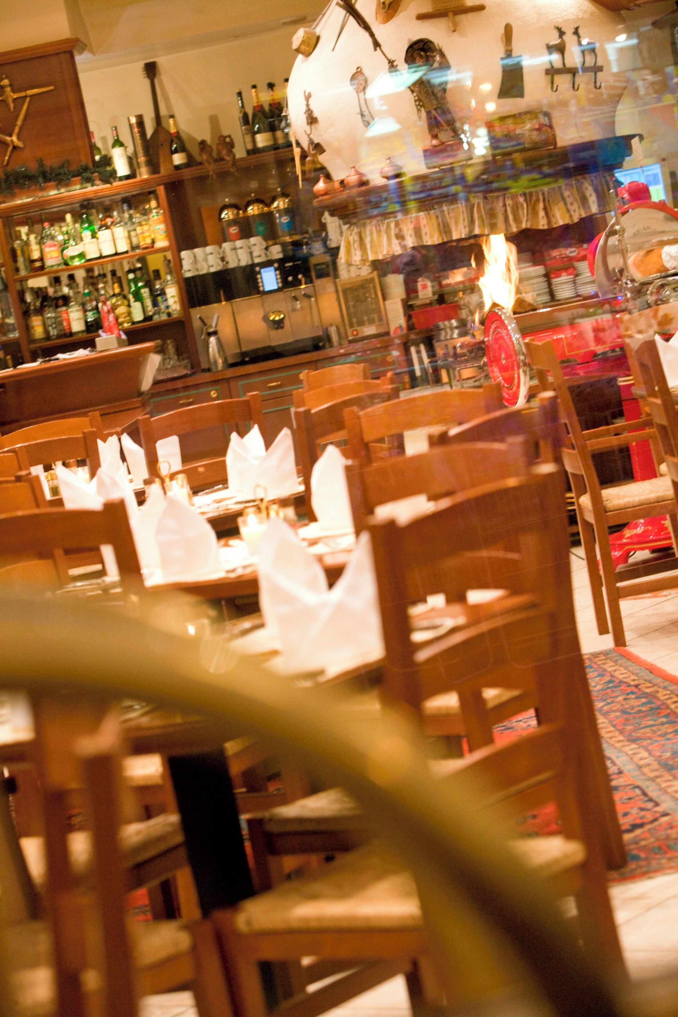 A restaurant interior with wooden tables and chairs, a bar area with bottles, and a decorative ceiling.