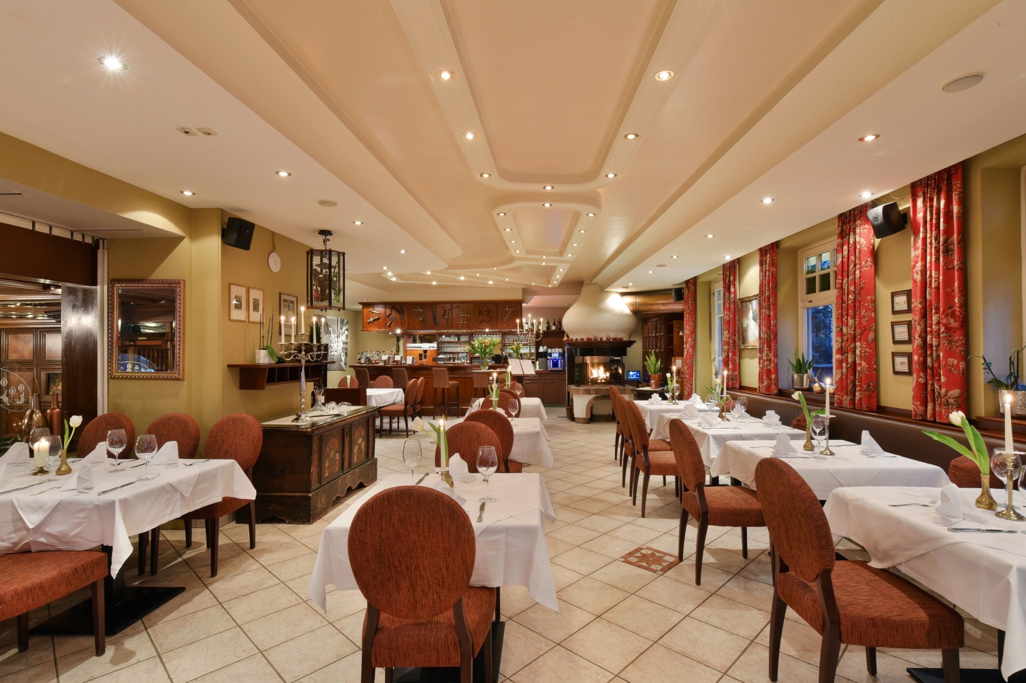 A restaurant with multiple tables and chairs, a bar area, and a decorative ceiling.