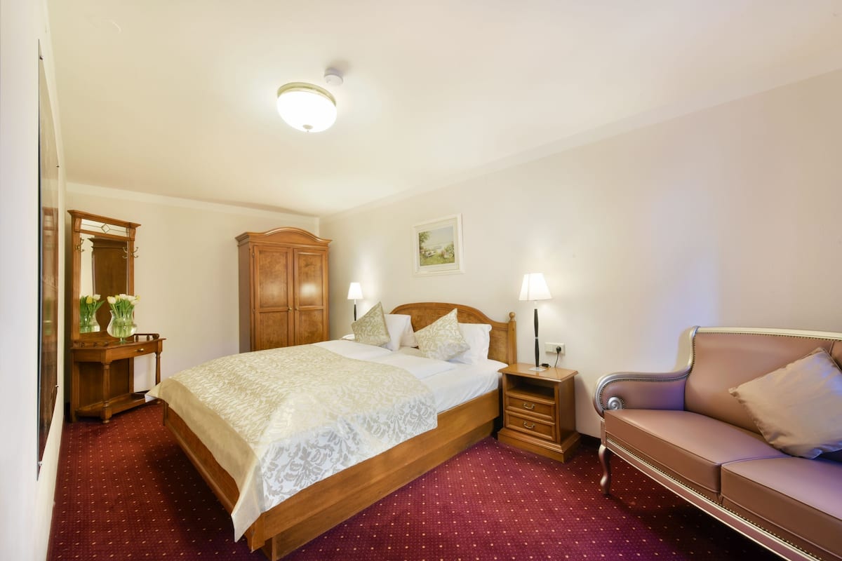 Une chambre d’hôtel avec un grand lit, des tables de chevet, une armoire en bois, un miroir et une moquette rouge.